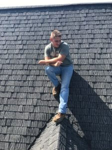 worker sitting on top of roof with black shingles